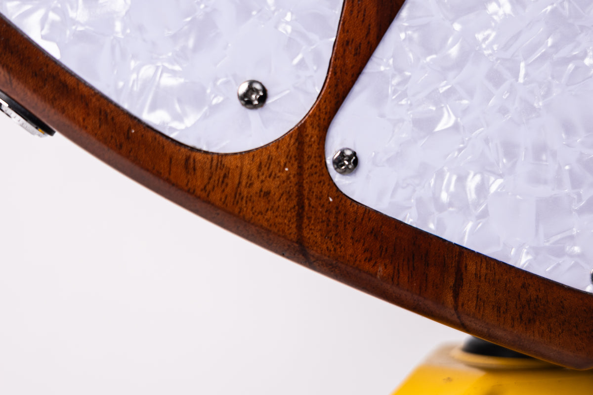 Close-up detail of an electric guitar body showing a rich dark brown wood grain frame with white pickguard inserts and two silver control plate screws.